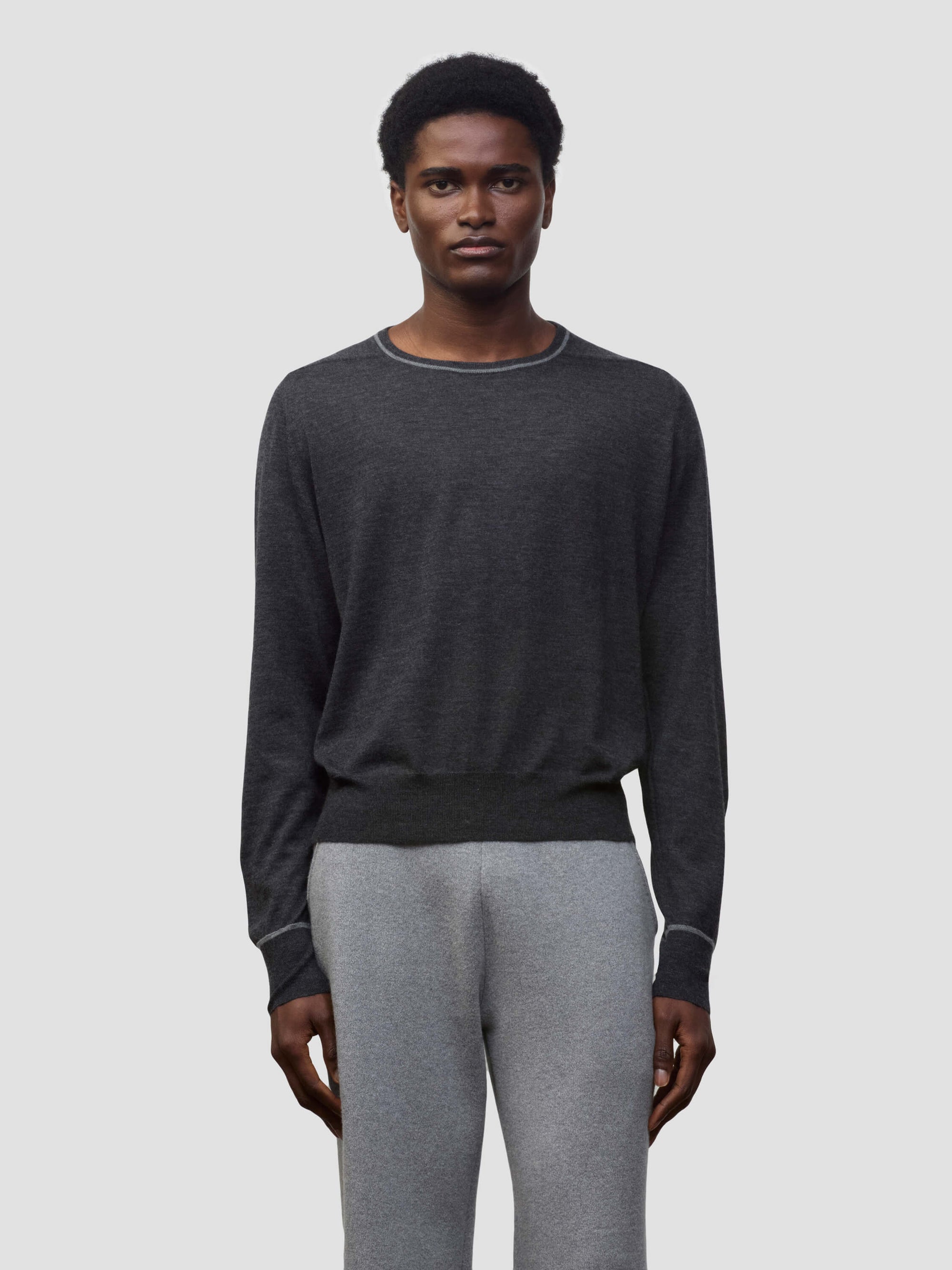 Person wearing a dark gray cashmere sweater and light gray cashmere pants on a plain background
