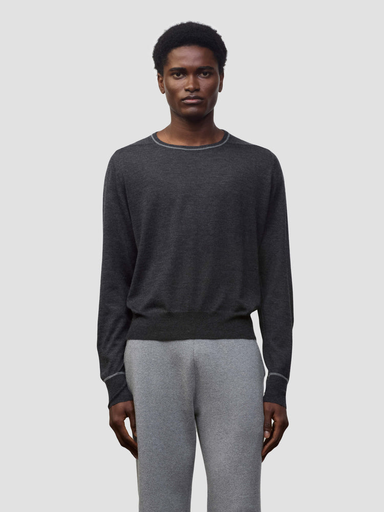 Person wearing a dark gray cashmere sweater and light gray cashmere pants on a plain background