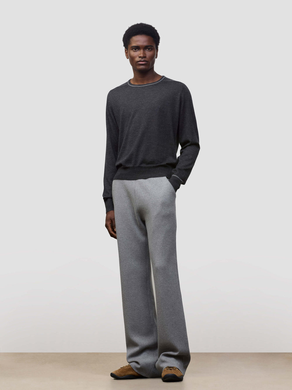 Person wearing a dark gray cashmere sweater and light gray cashmere pants on a plain background