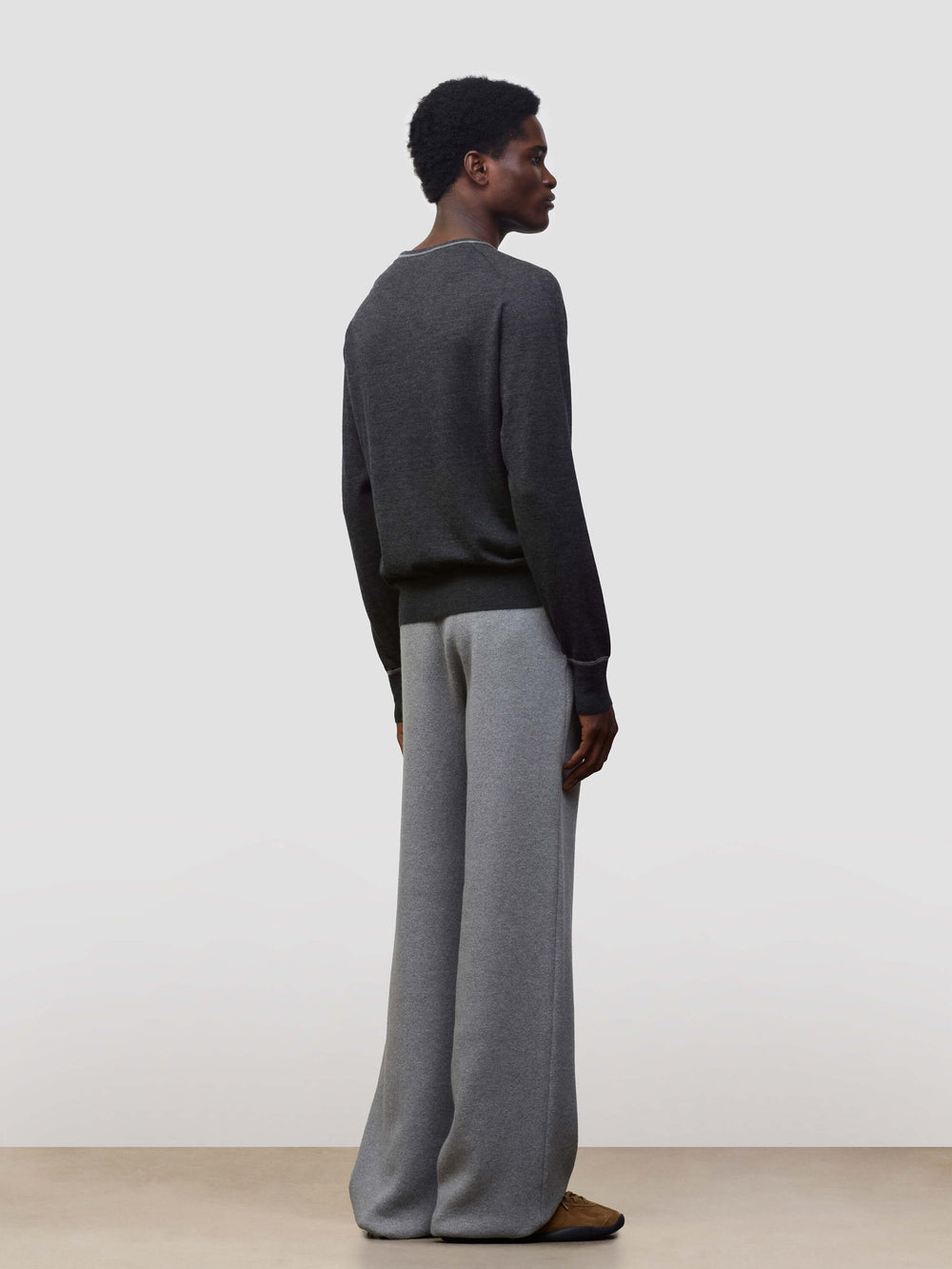 Person wearing a dark gray cashmere sweater and light gray cashmere pants on a plain background