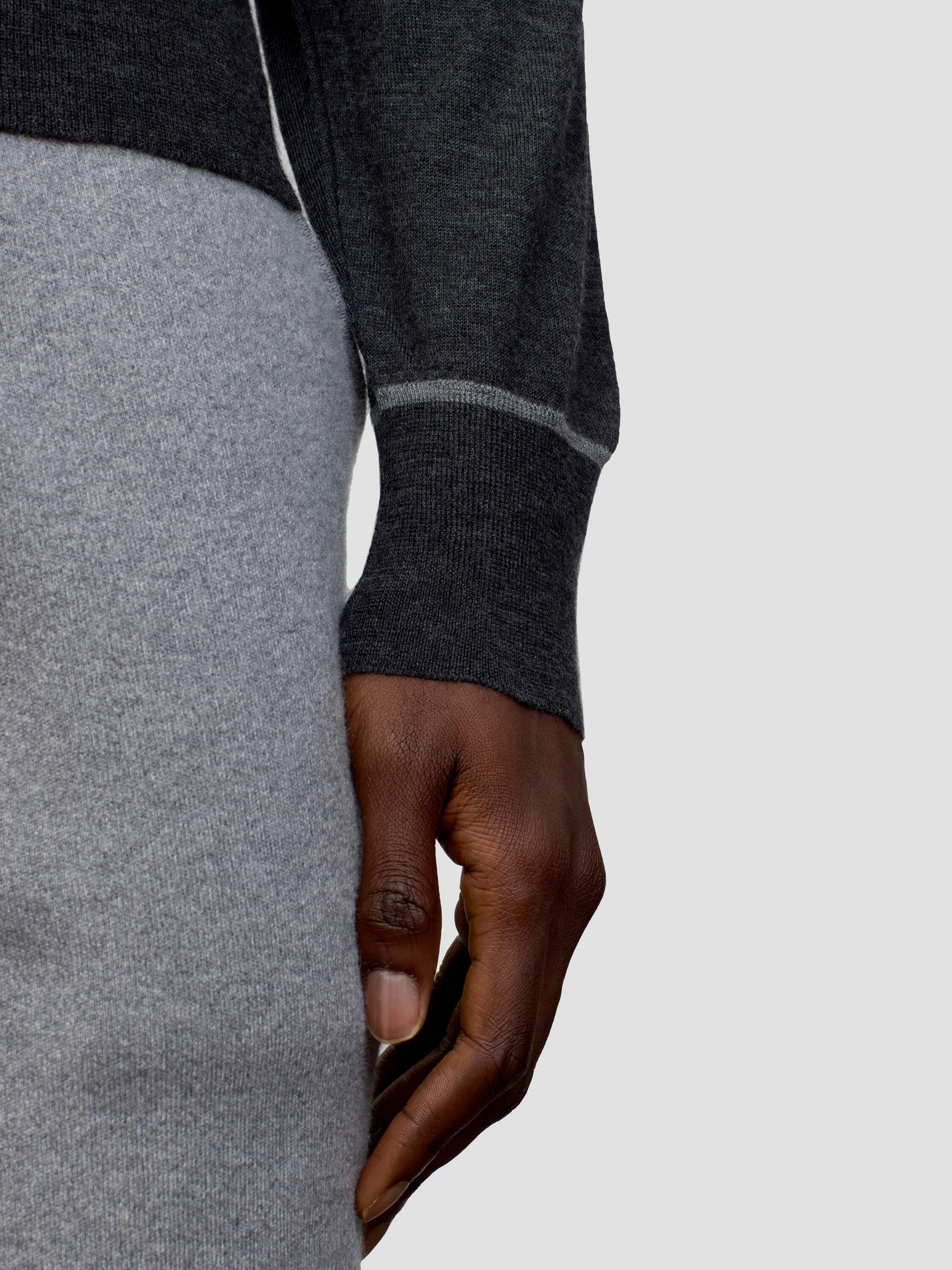 Person wearing a dark gray cashmere sweater and light gray cashmere pants on a plain background