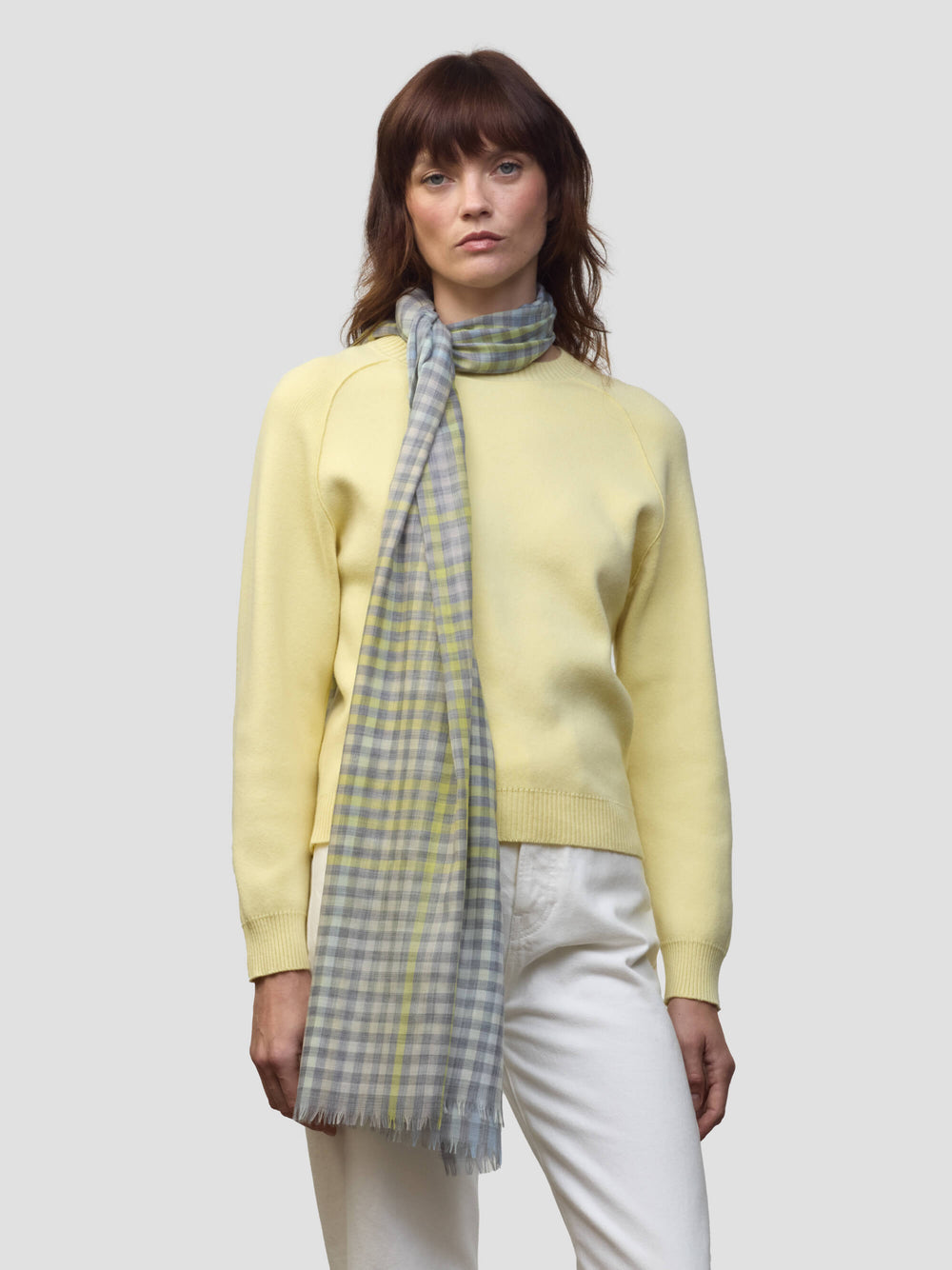 woman wearing a yellow sweater with grey and yellow check scarf on a grey background