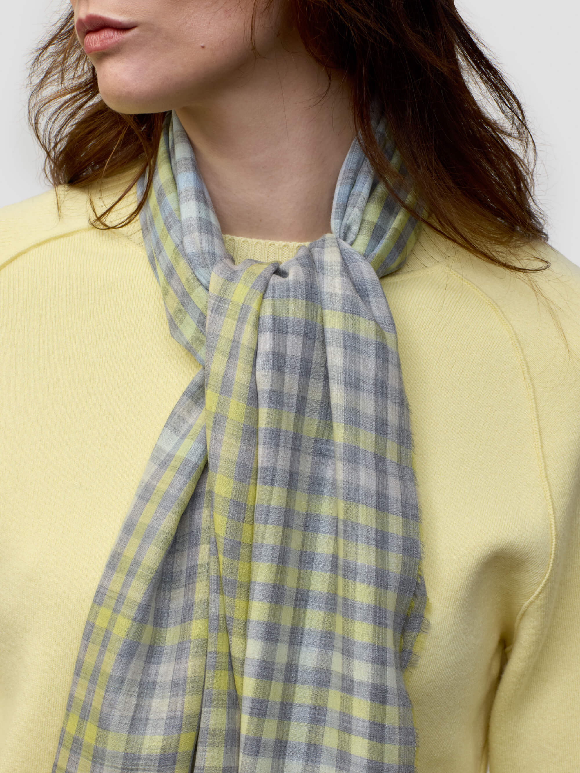 woman wearing a yellow sweater with grey and yellow check scarf on a grey background