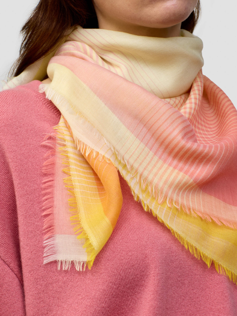 woman wearing a pink cashmere sweater with yellow and orange patterned scarf on a grey background