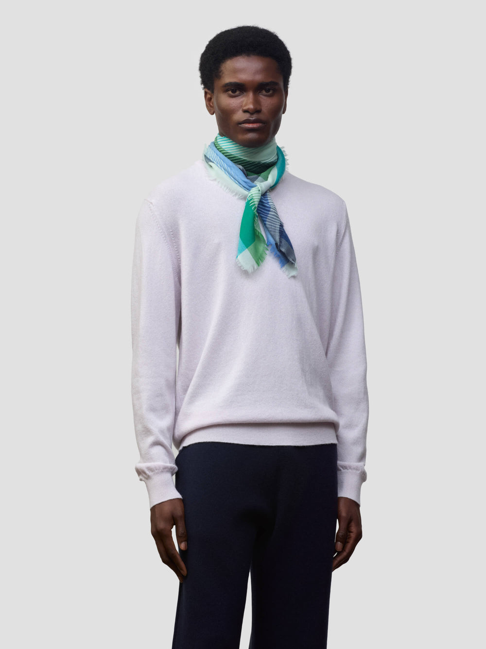 man wearing a lilac cashmere sweater with green and blue patterned neck scarf on a grey background
