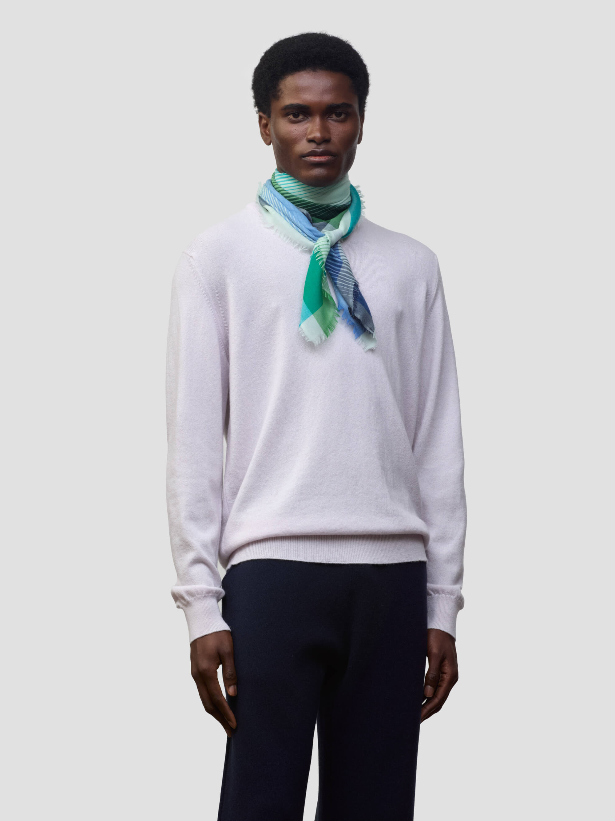 man wearing a lilac cashmere sweater with green and blue patterned neck scarf on a grey background