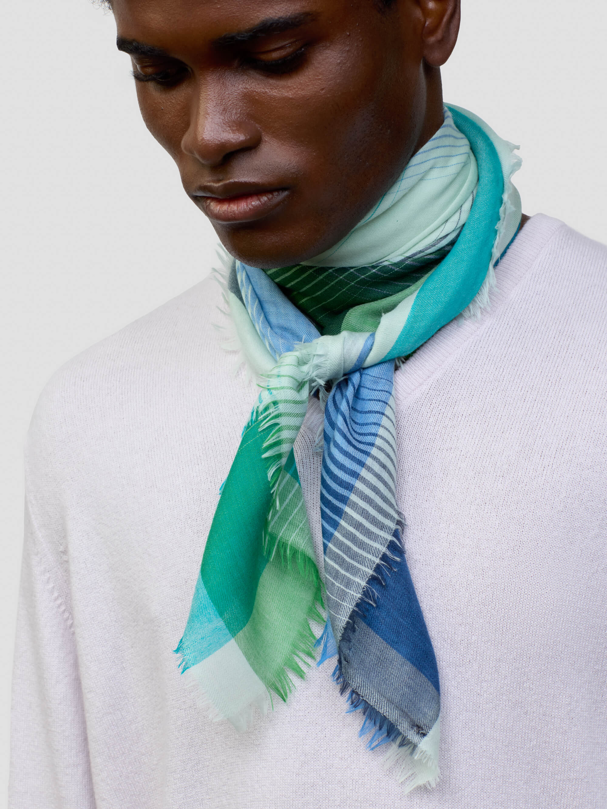 man wearing a lilac cashmere sweater with green and blue patterned neck scarf on a grey background