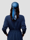 woman wearing a long navy cashmere coat and matching navy and blue patterned scarf tied around head on a grey background