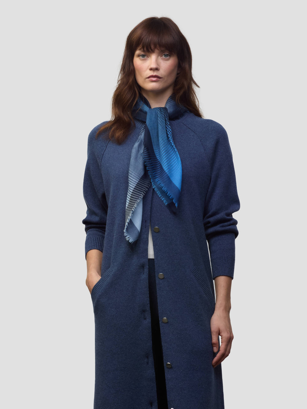 woman wearing a long navy cashmere coat and matching navy and blue patterned scarf on a grey background