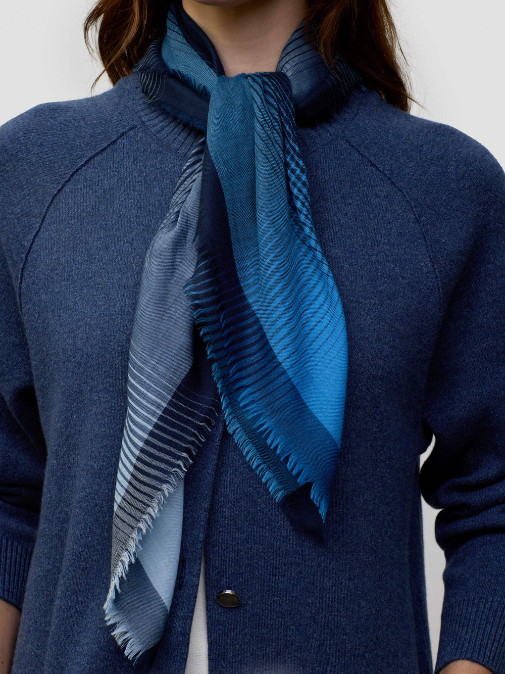 close up of a woman wearing a long navy cashmere coat and matching navy and blue patterned scarf on a grey background