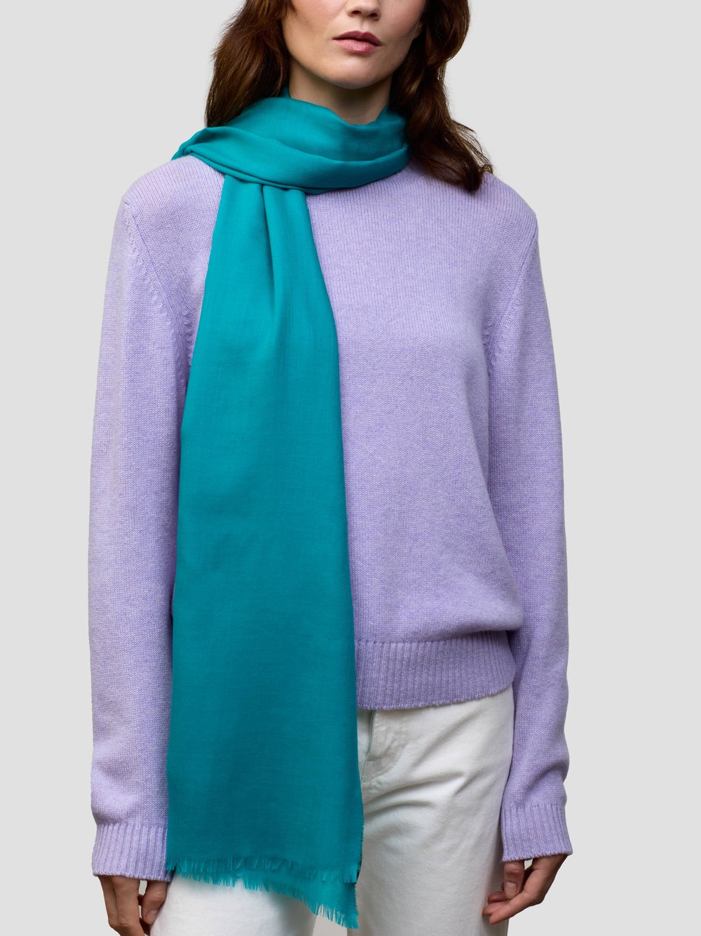 women wearing a lilac cashmere sweater and teal scarf with white trousers on a grey background