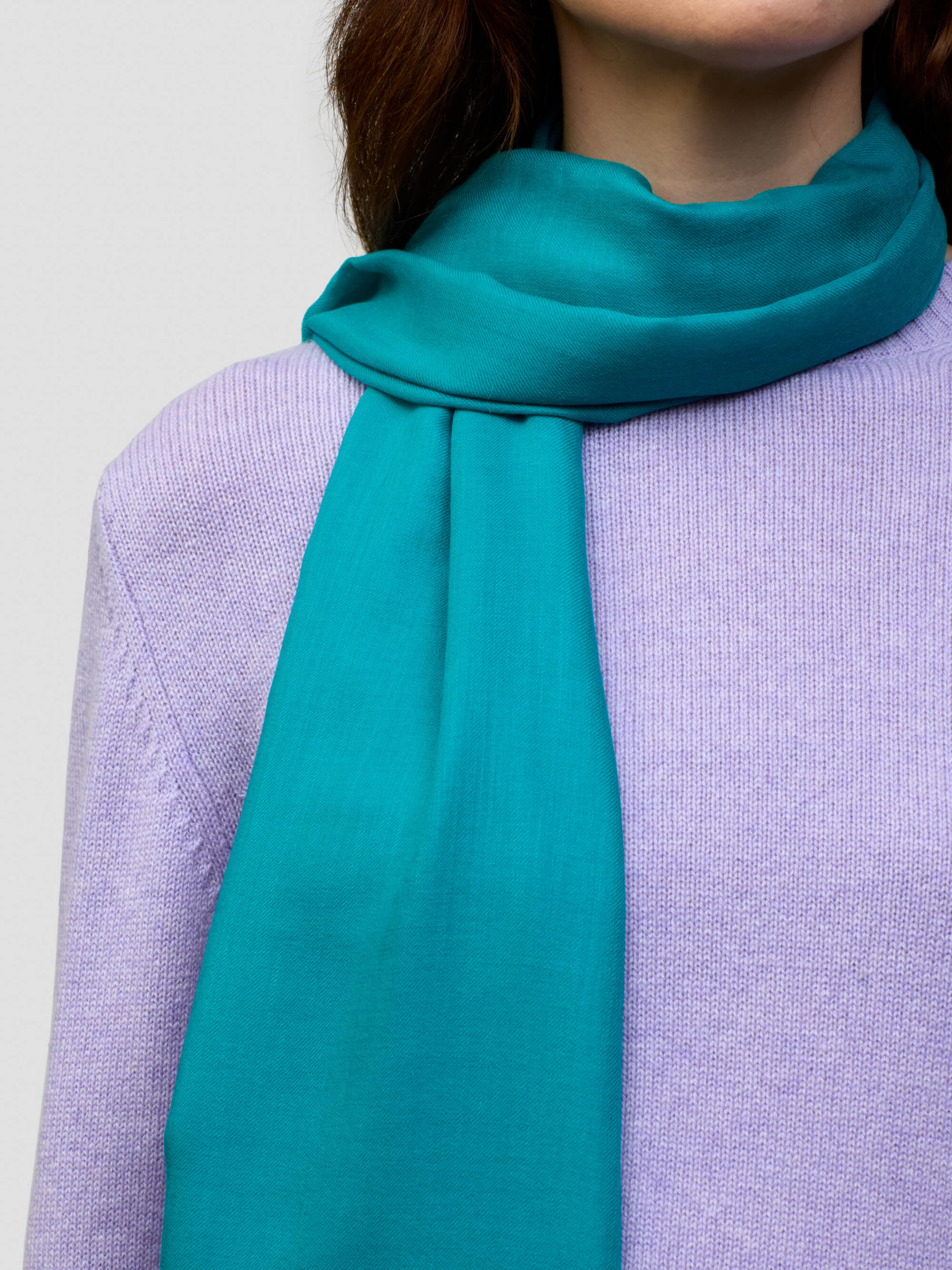 women wearing a lilac cashmere sweater and teal scarf on a grey background