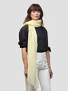 women wearing a black shirt with light yellow cashmere scarf and white trousers on a grey background