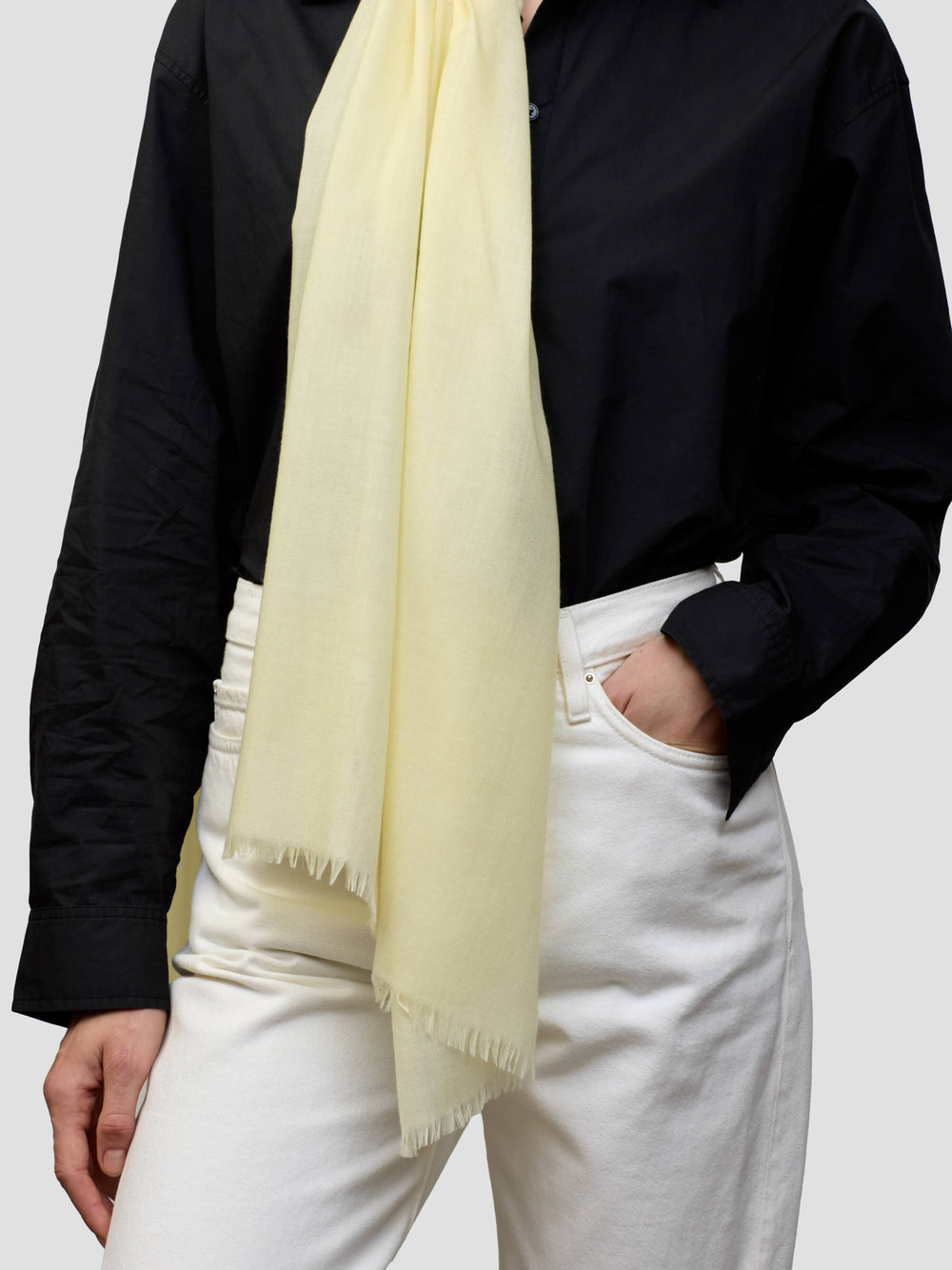 women wearing a black shirt with light yellow cashmere scarf and white trousers on a grey background