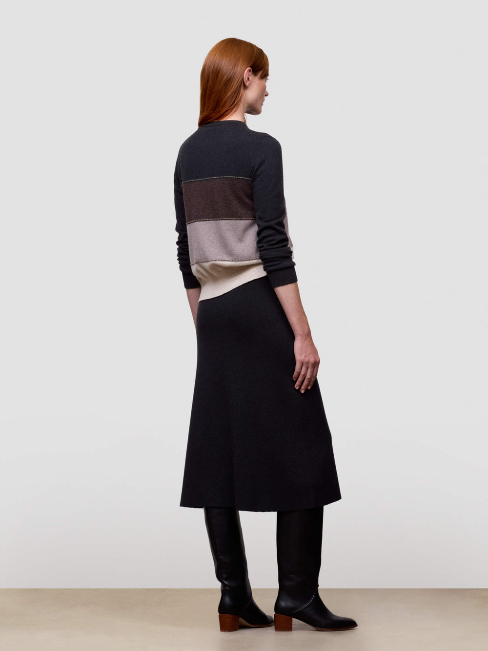 Woman wearing a long, dark-colored cashmere dress with a color-blocked top against a plain background