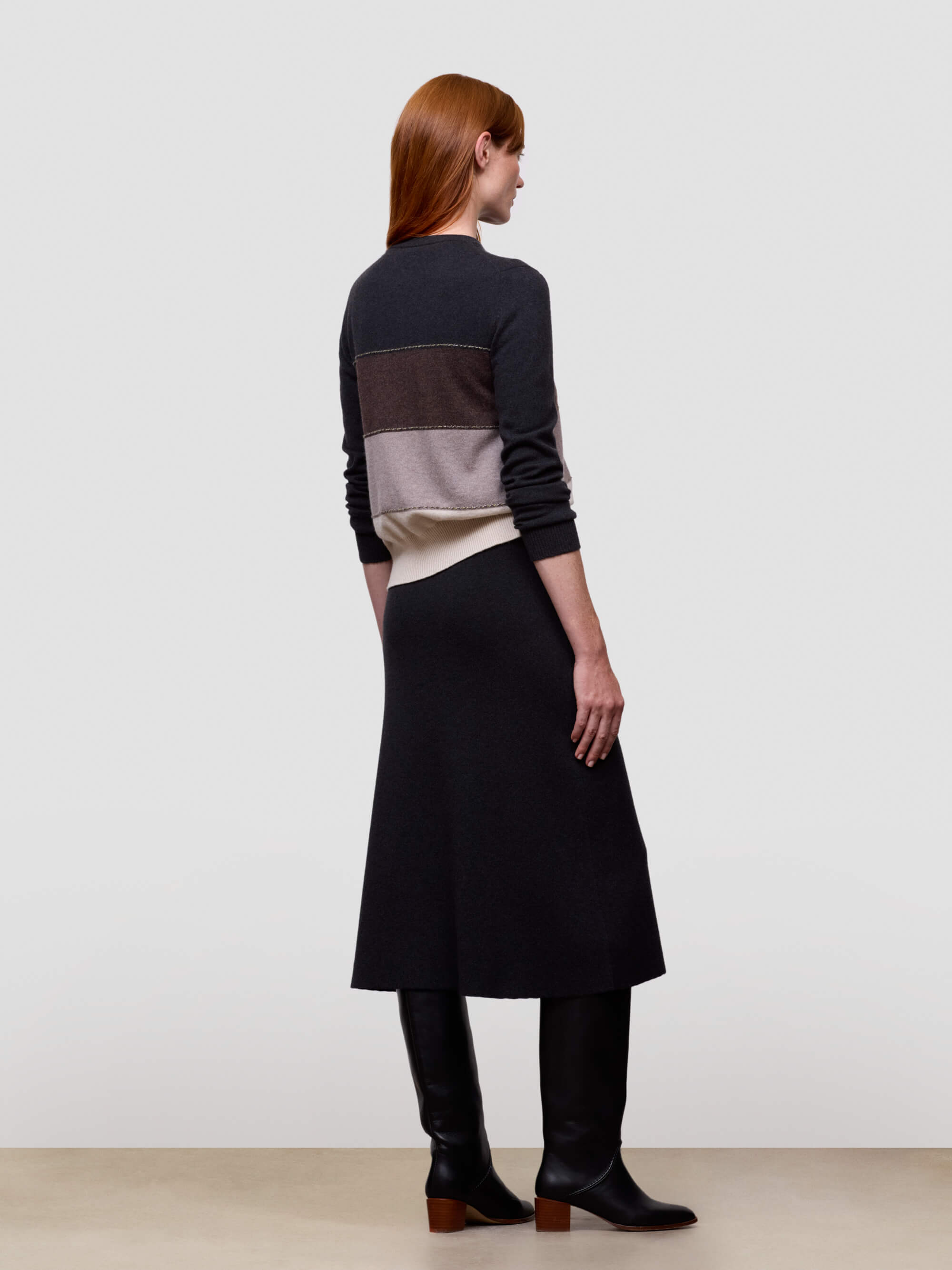 Woman wearing a long, dark-colored cashmere dress with a color-blocked top against a plain background