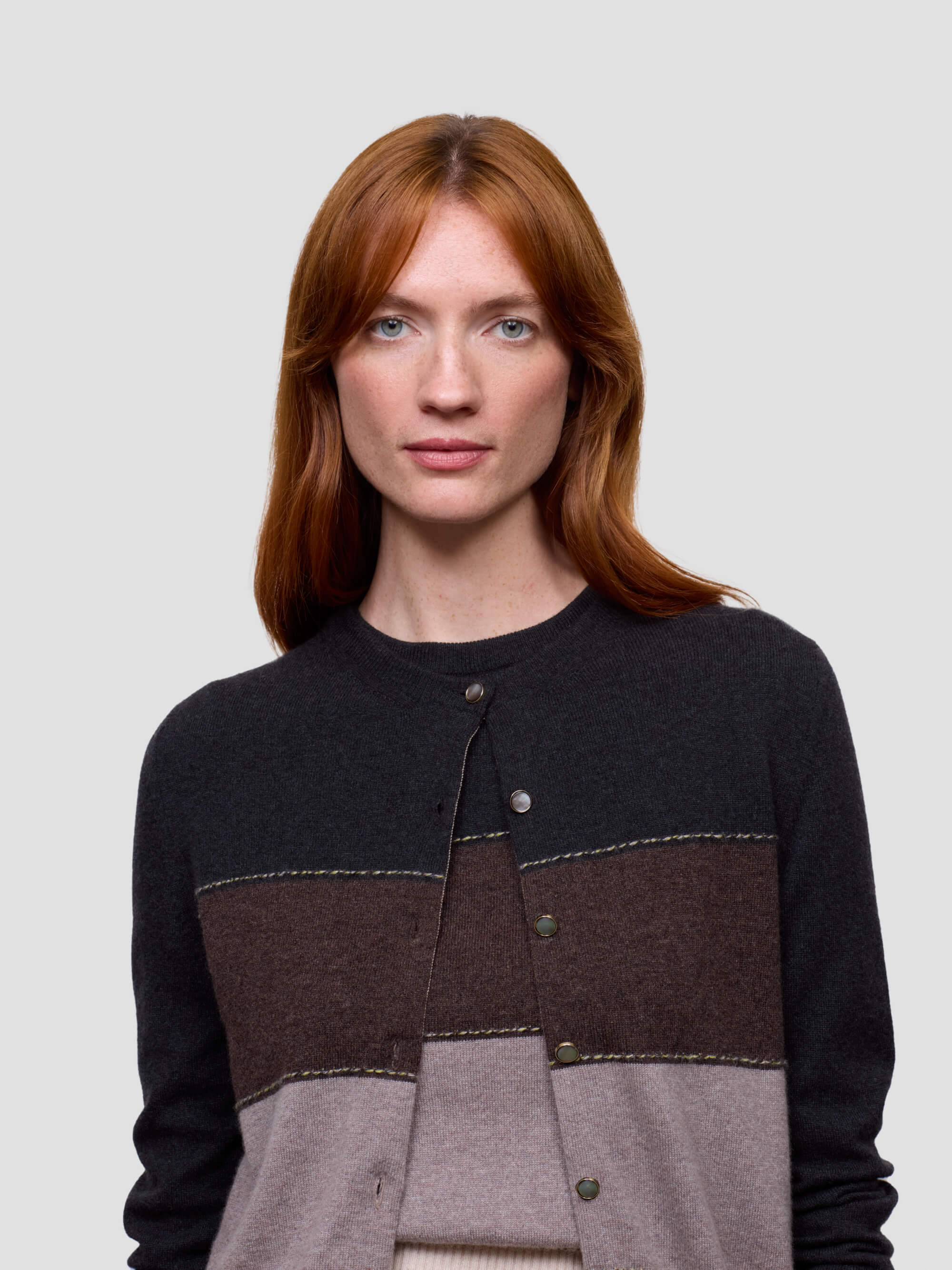 Woman wearing a black, brown, and gray color-blocked cashmere sweater on a light gray background