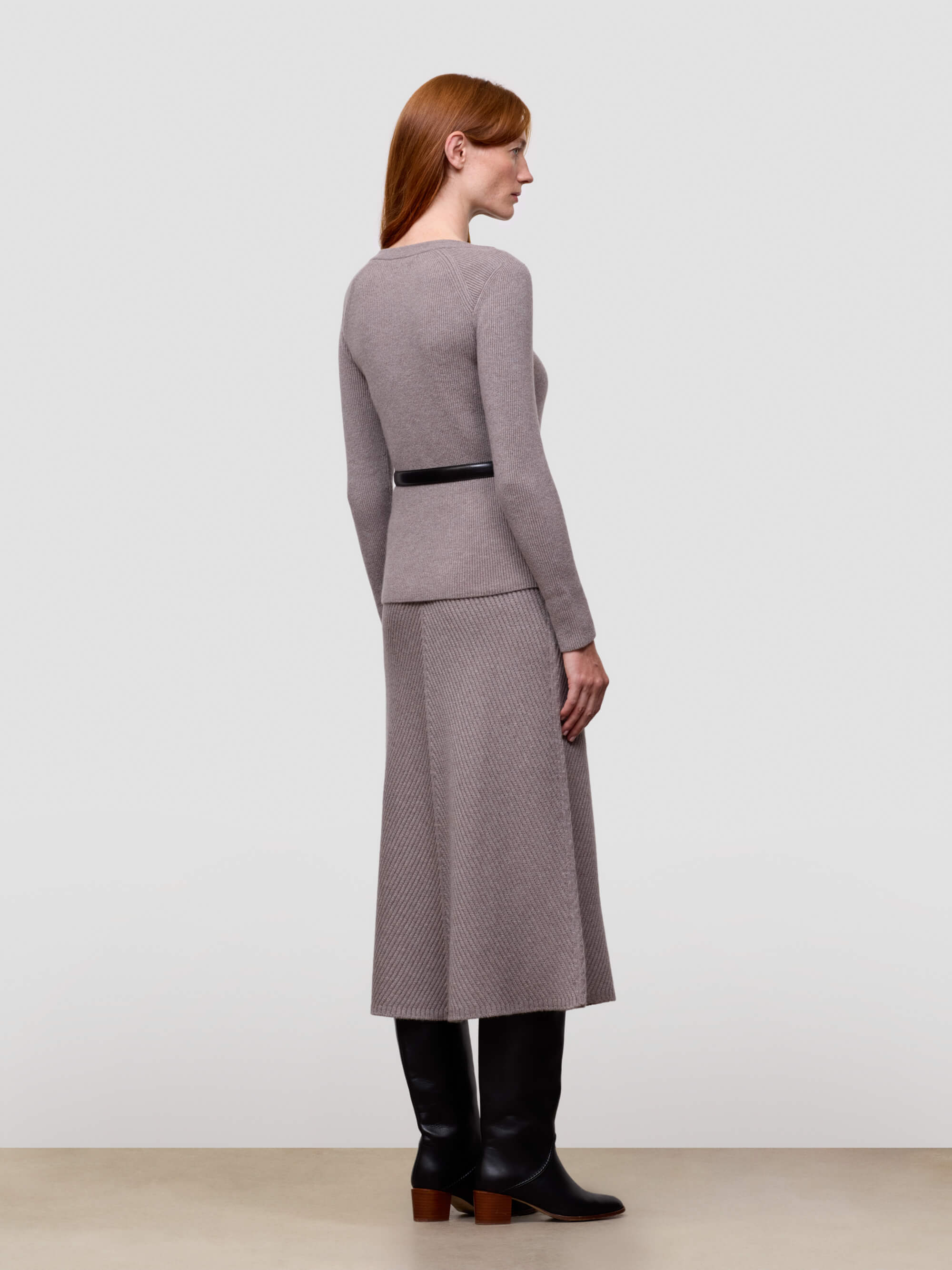 Woman wearing a gray cashmere sweater and skirt set with a black belt on a light gray background