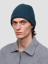 Man wearing a green knit cashmere beanie and gray sweater against a plain background