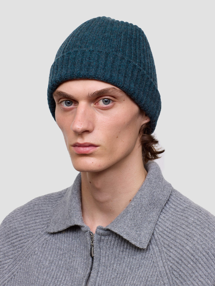 Man wearing a green knit cashmere beanie and gray sweater against a plain background