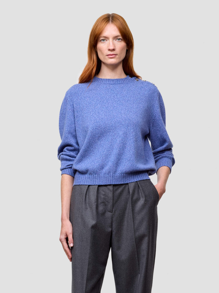 Woman wearing a blue cashmere sweater and gray pants on a light gray background