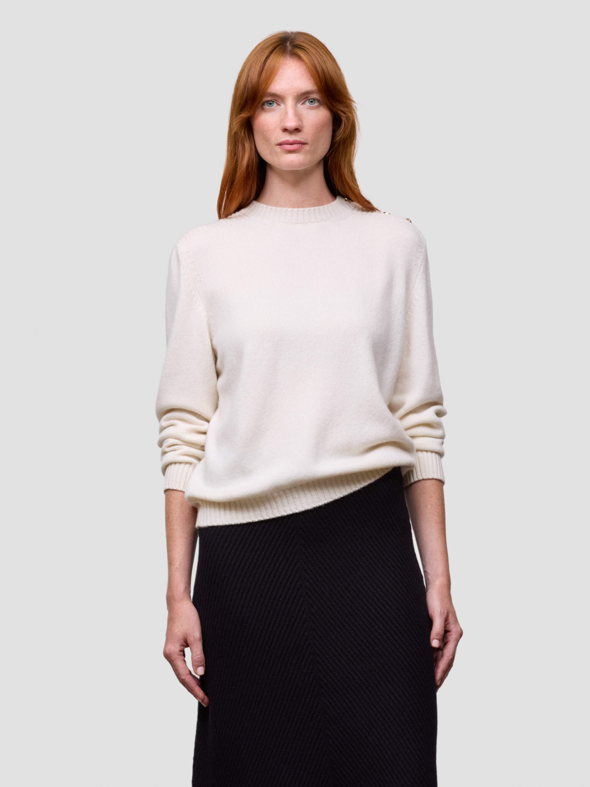Woman wearing a white cashmere sweater and black skirt on a light gray background