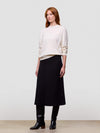 Woman wearing a white cashmere sweater and black cashmere skirt on a plain background