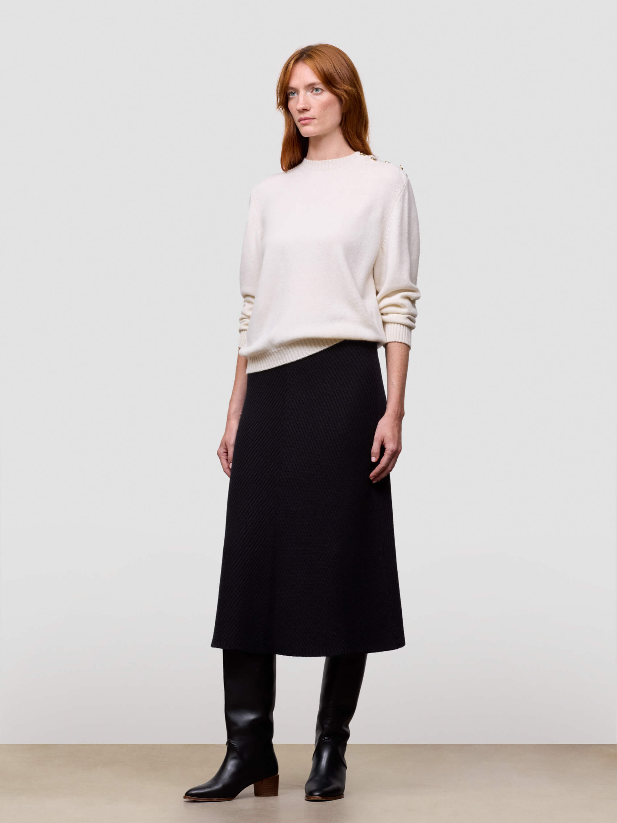 Woman wearing a white cashmere sweater and black cashmere skirt on a plain background
