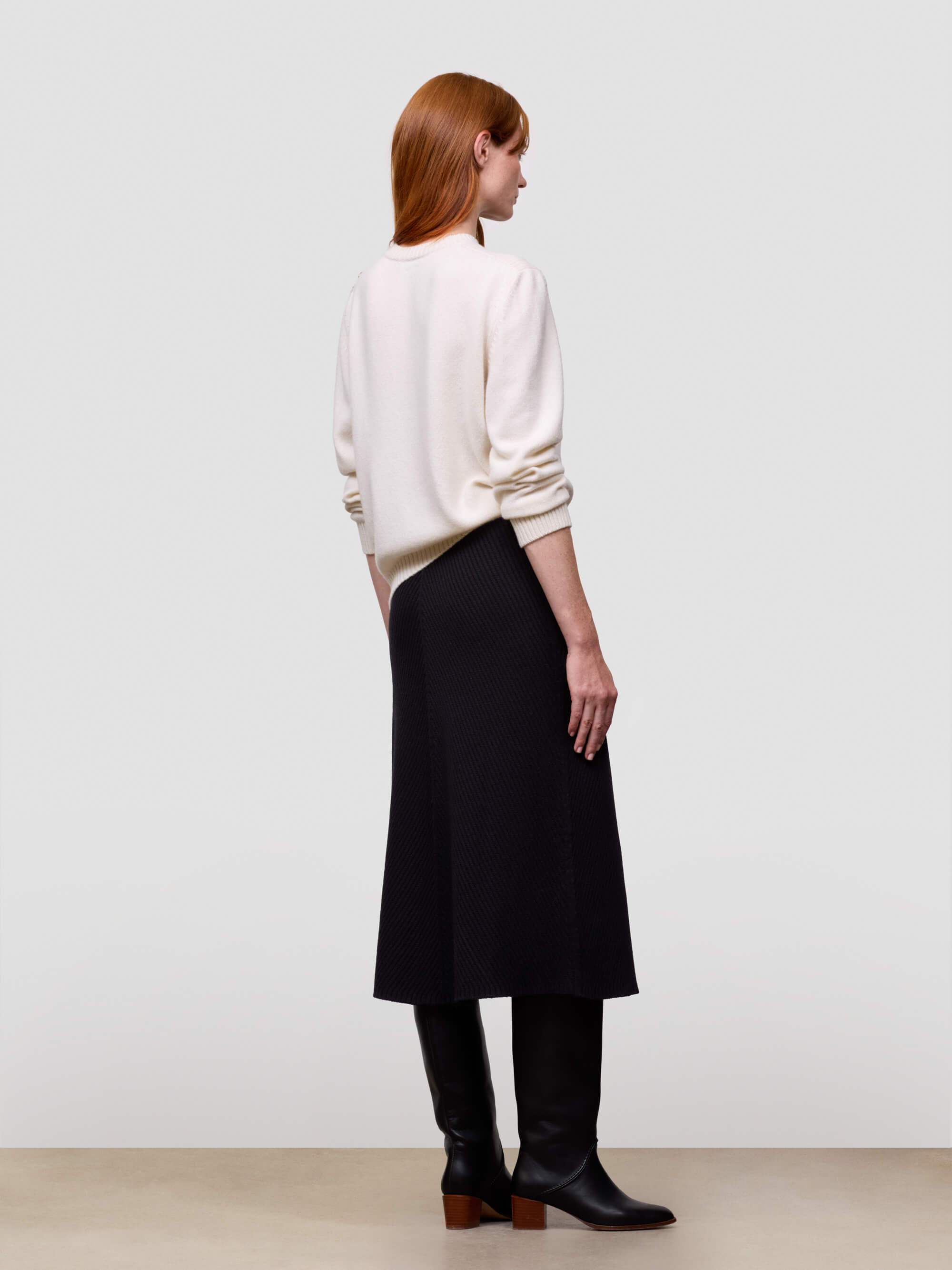 Woman wearing a white cashmere sweater and black cashmere skirt against a plain background