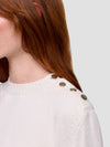Close-up of a woman wearing a white cashmere sweater with pearl buttons on a light gray background