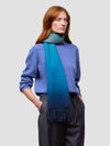 woman wearing a blue gradient cashmere scarf and blue cashmere sweater on a grey background