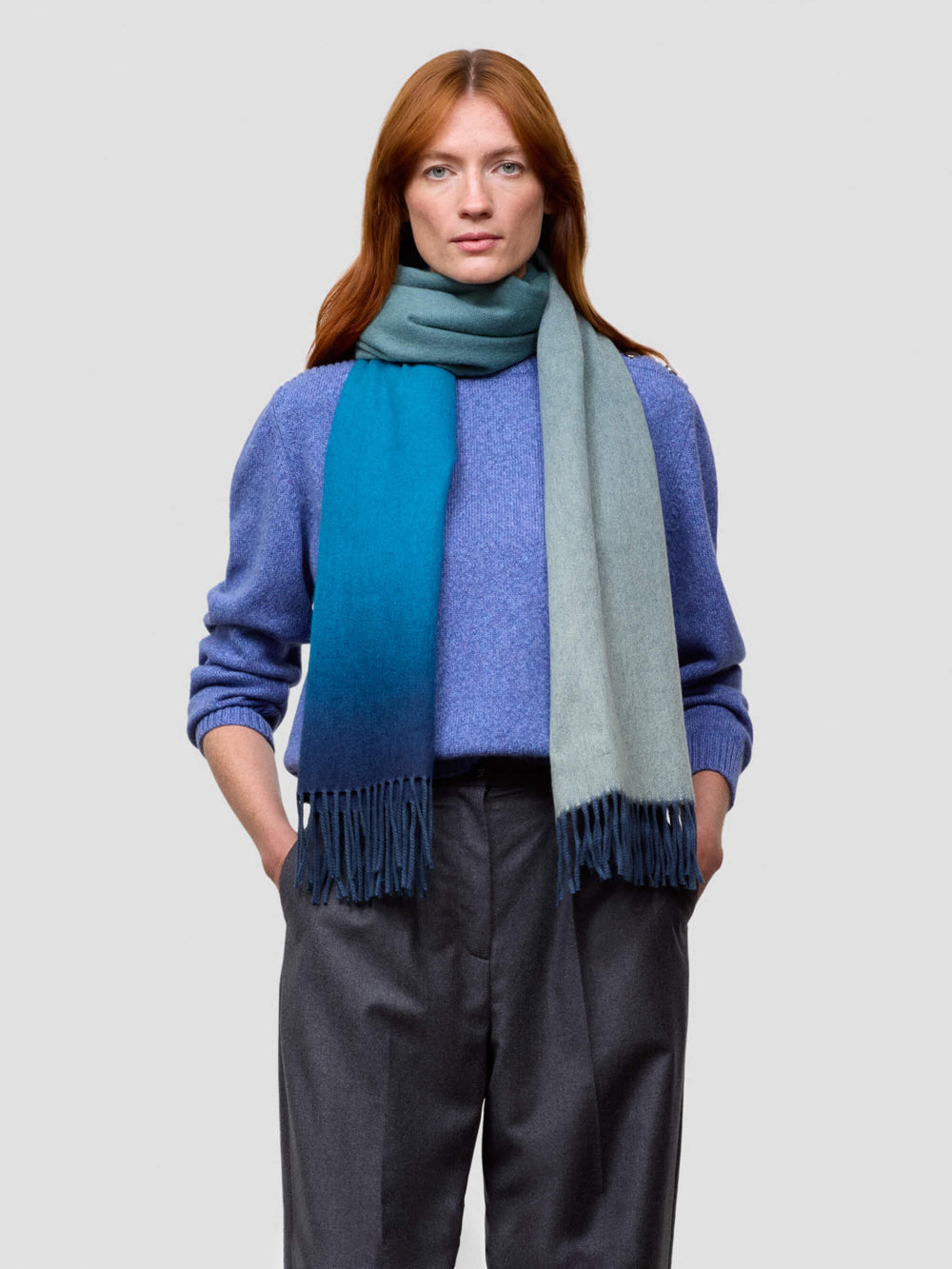 woman wearing a blue gradient cashmere scarf and blue cashmere sweater on a grey background
