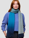 woman wearing a blue gradient cashmere scarf and blue cashmere sweater on a grey background