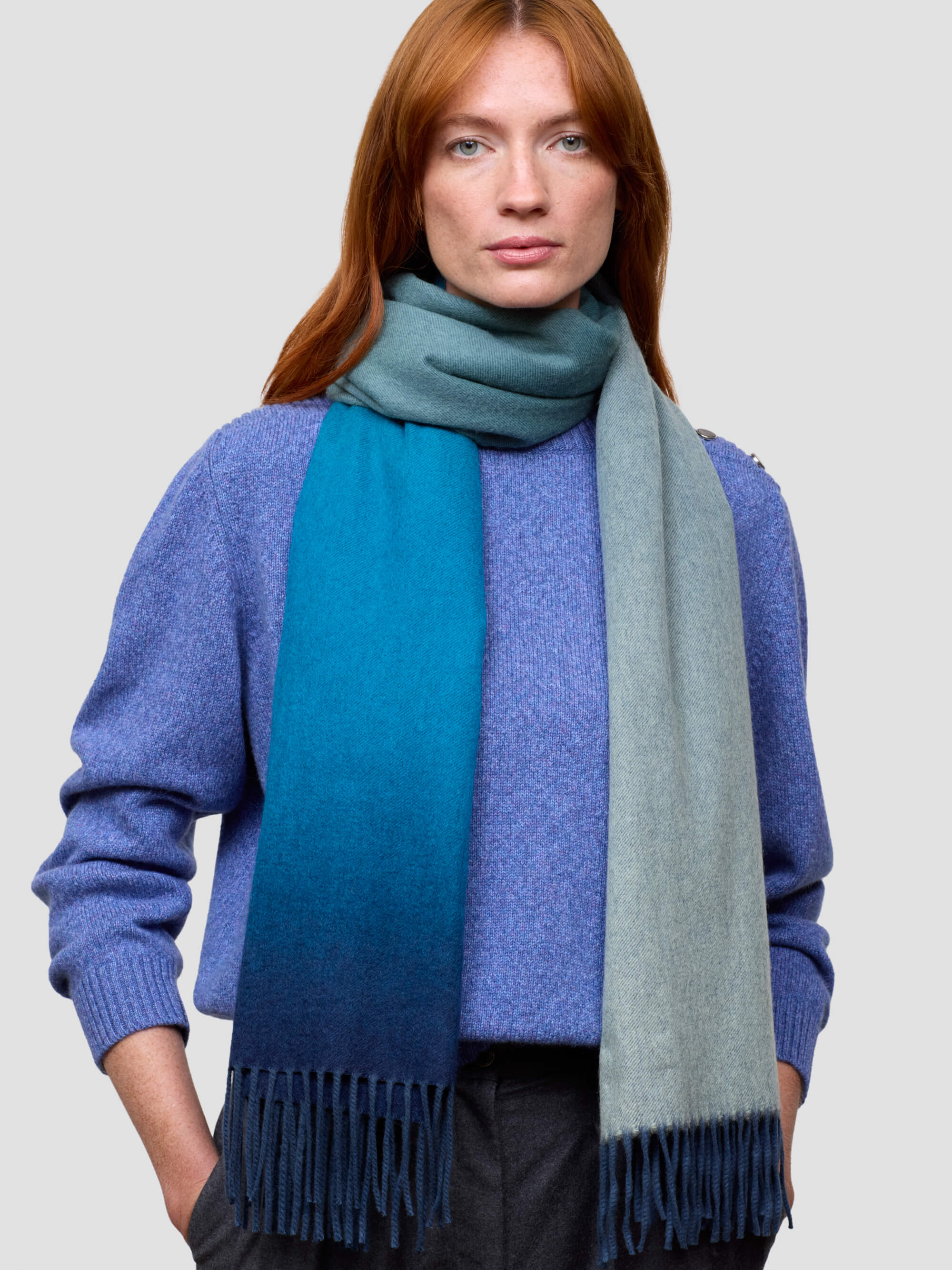 woman wearing a blue gradient cashmere scarf and blue cashmere sweater on a grey background