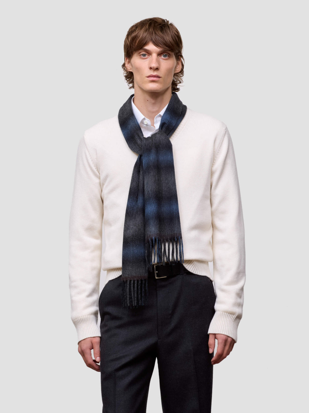 Man wearing a blue and black tartan cashmere scarf on a plain background