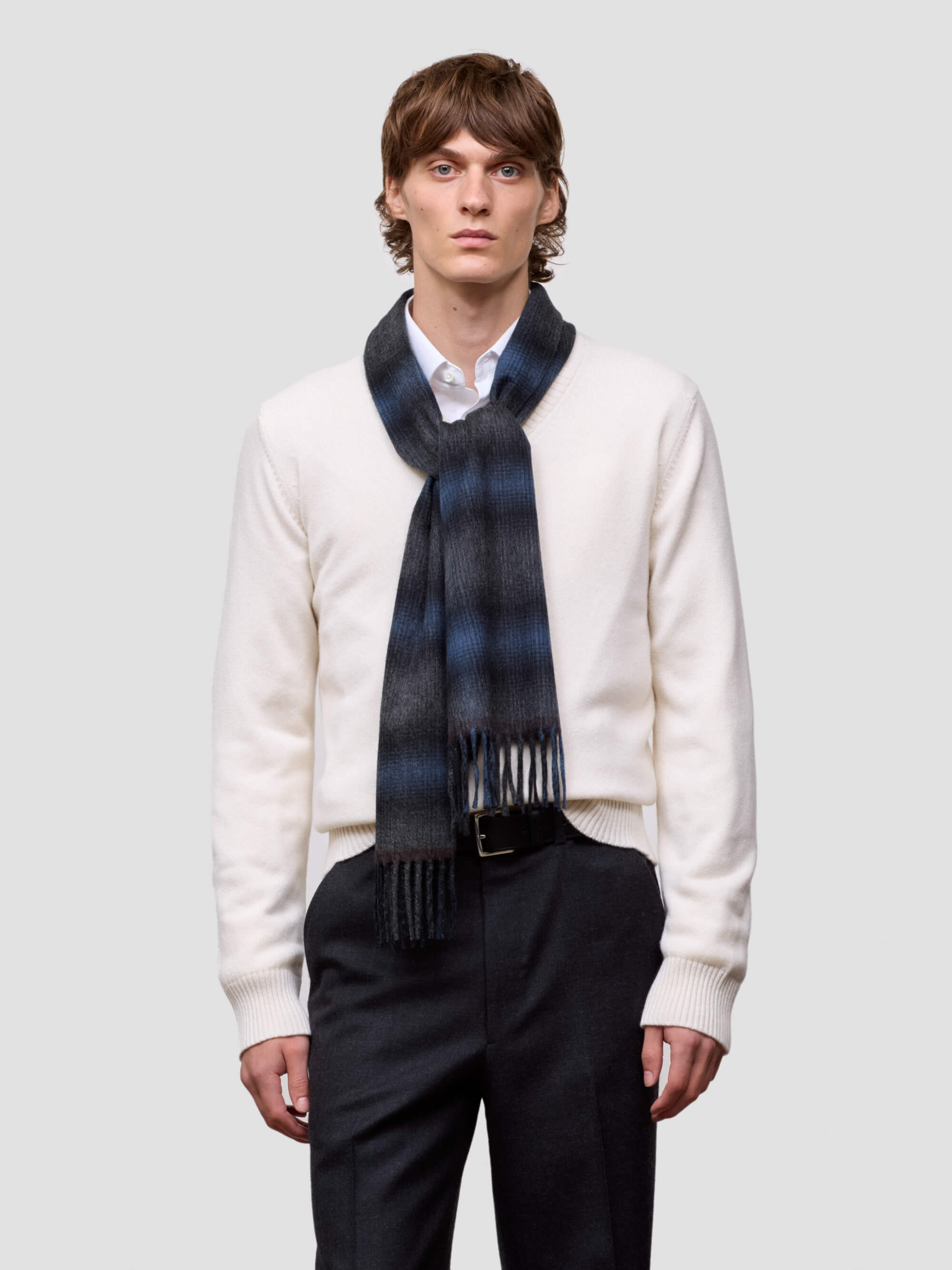 Man wearing a blue and black tartan cashmere scarf on a plain background