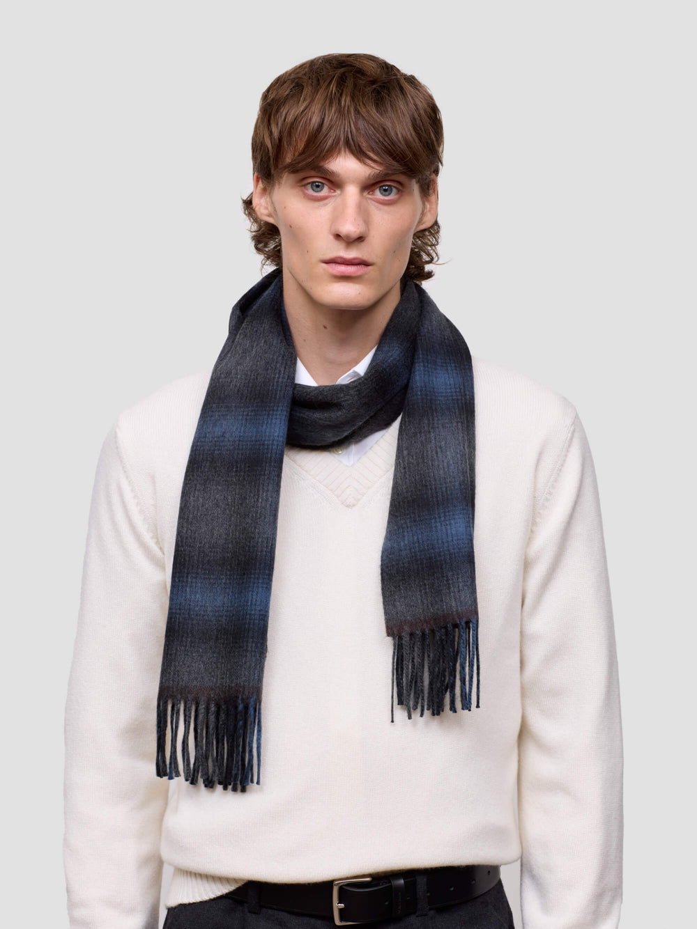 Man wearing a blue and black plaid scarf on a plain background
