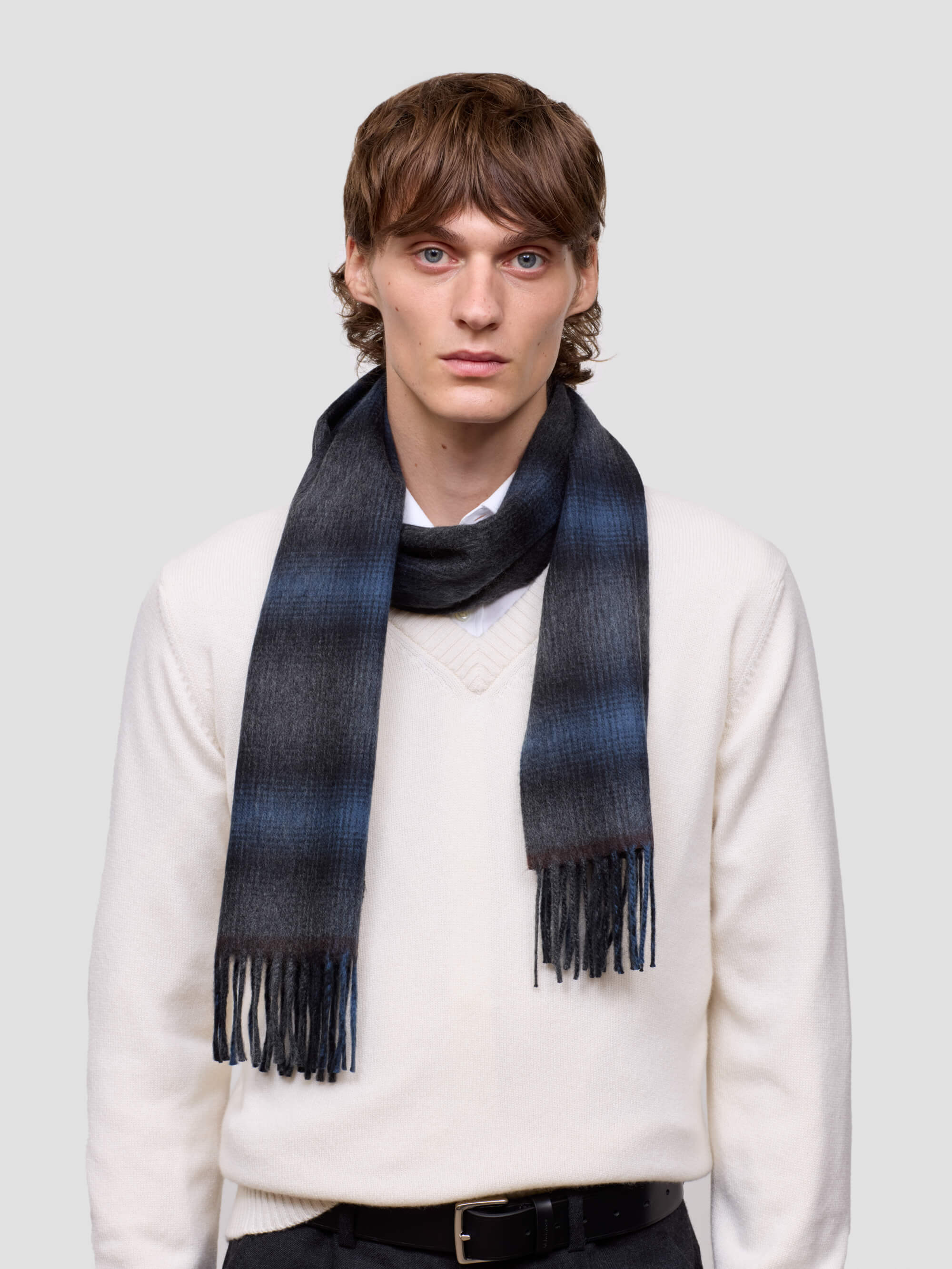 Man wearing a blue and black plaid scarf on a plain background