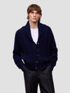 Man wearing a navy blue cashmere cardigan over a white shirt on a light gray background