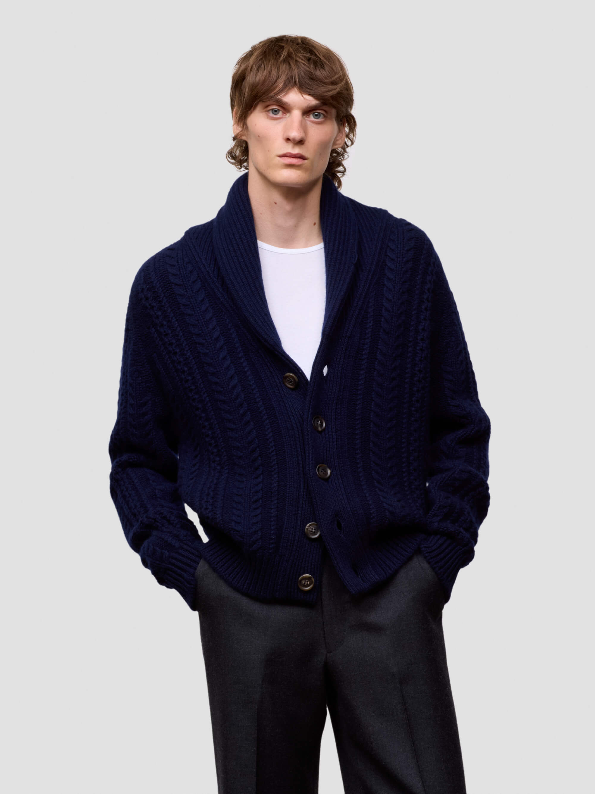 Man wearing a navy blue cashmere cardigan over a white shirt on a light gray background