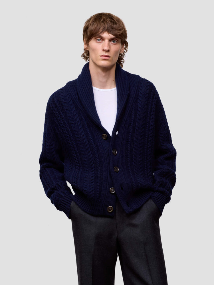 Man wearing a navy blue cashmere cardigan over a white shirt on a light gray background