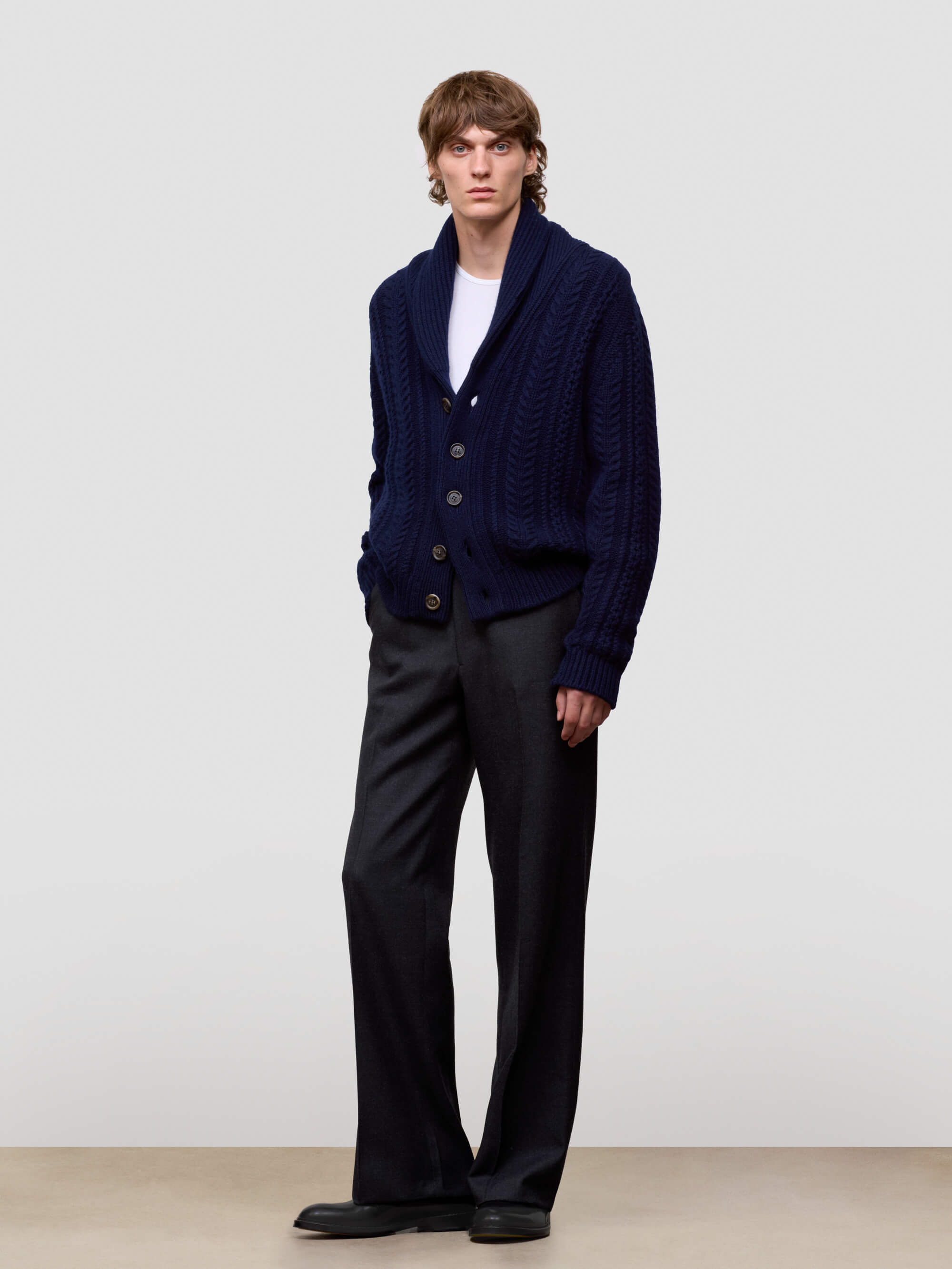 Man wearing a navy blue cashmere cardigan over a white shirt on a light gray background