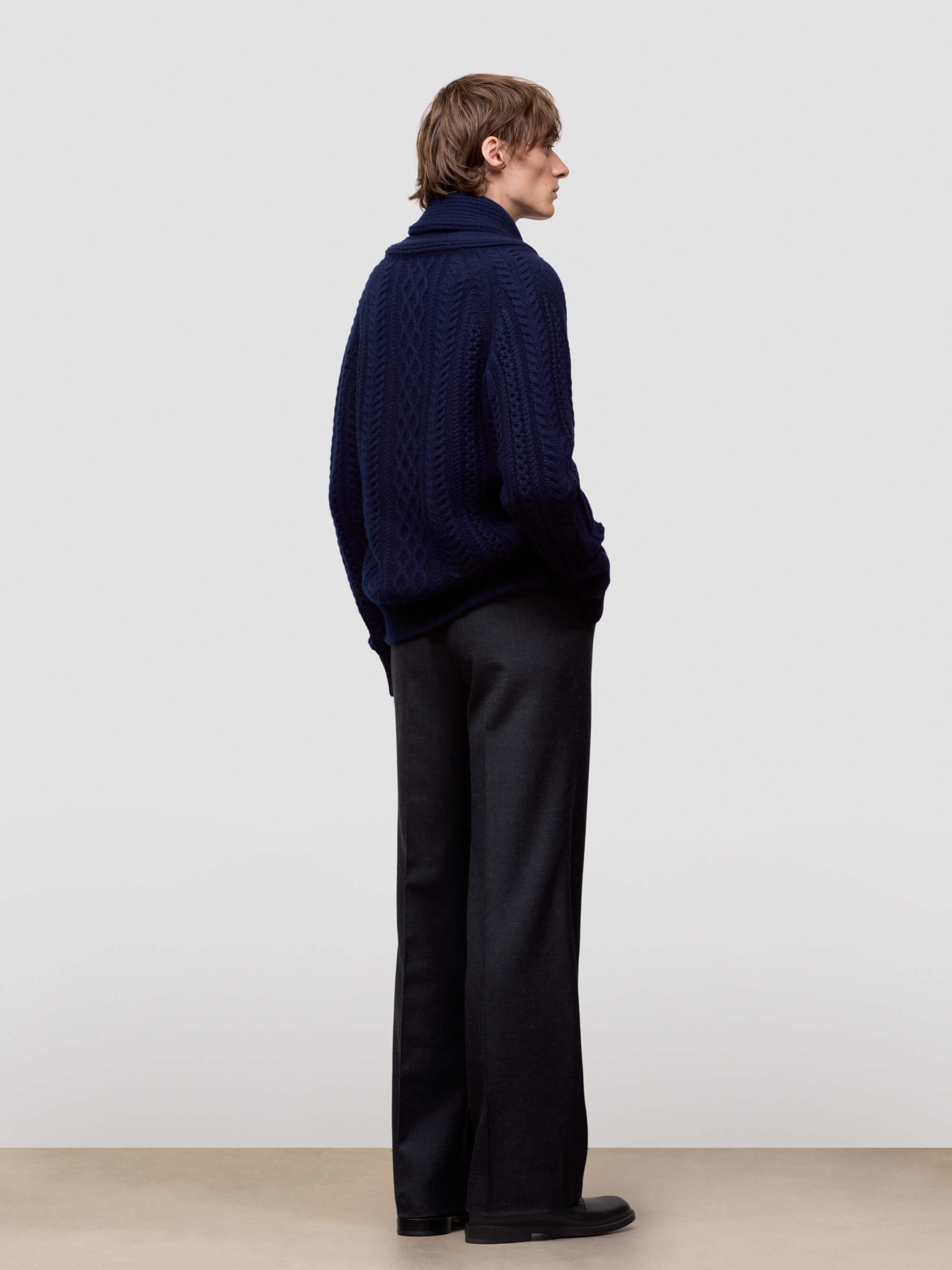 Man wearing a navy blue cashmere cardigan over a white shirt on a light gray background