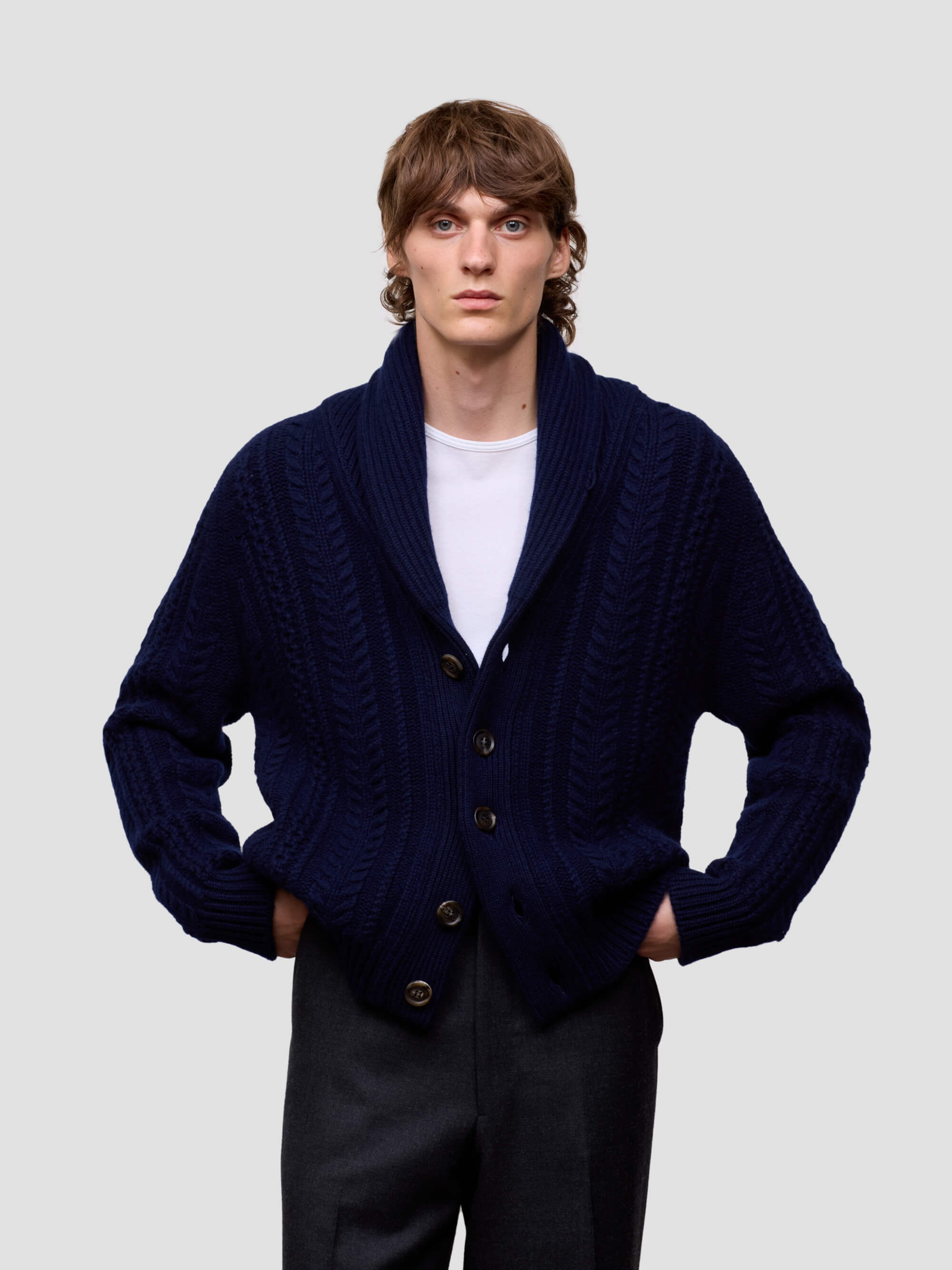Man wearing a navy blue cashmere cardigan over a white shirt on a light gray background