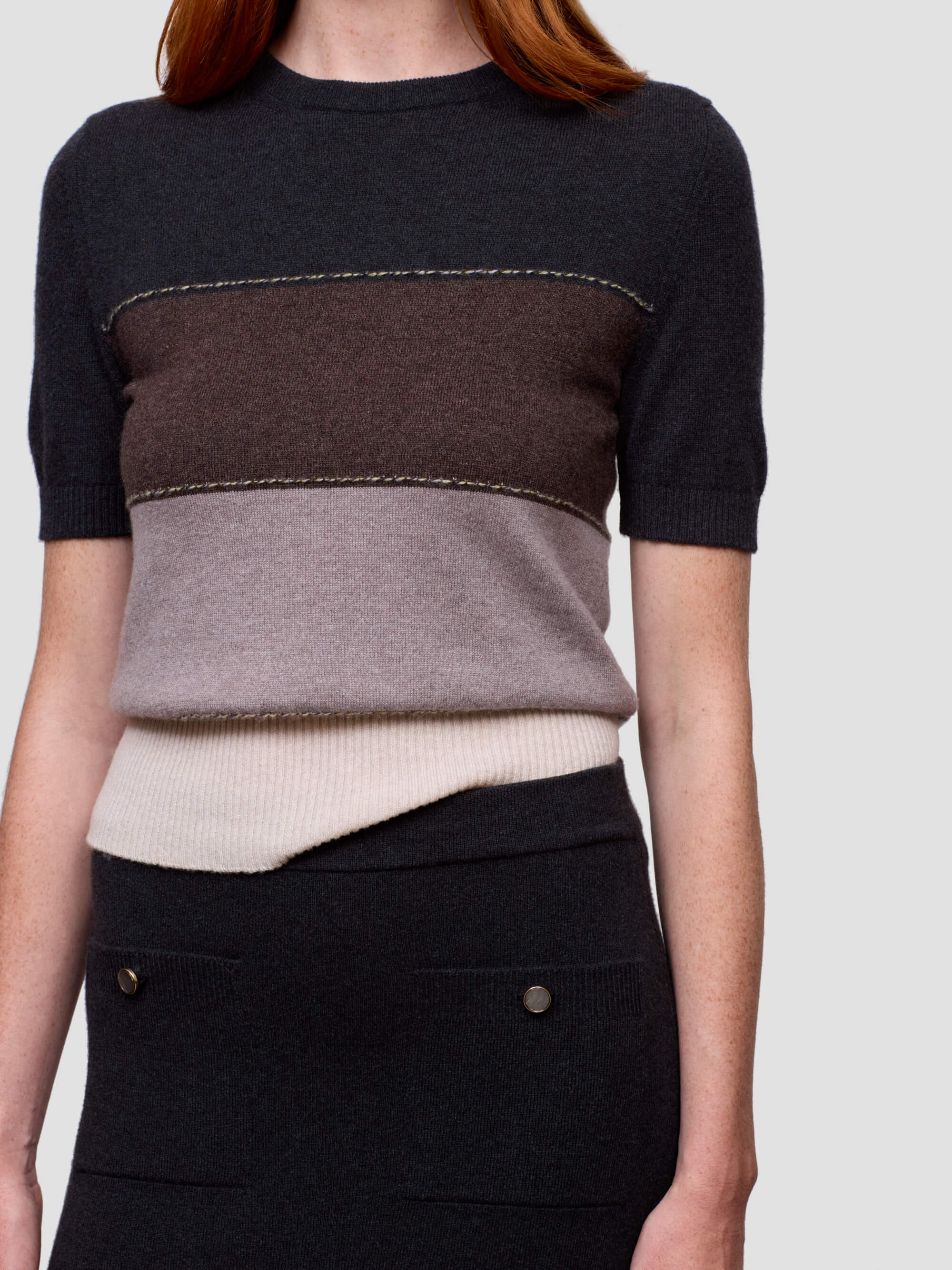 Woman wearing a black, brown, and beige color-blocked cashmere t-shirt on a light gray background