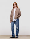 Woman wearing a brown cashmere cardigan over a white shirt and blue jeans on a light gray background