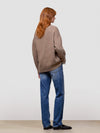 Woman wearing a brown cashmere cardigan over a white shirt and blue jeans on a light gray background
