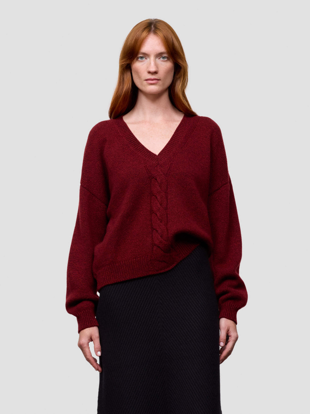 woman wearing a red chunky v-neck cashmere sweater and black cashmere skirt on a grey background