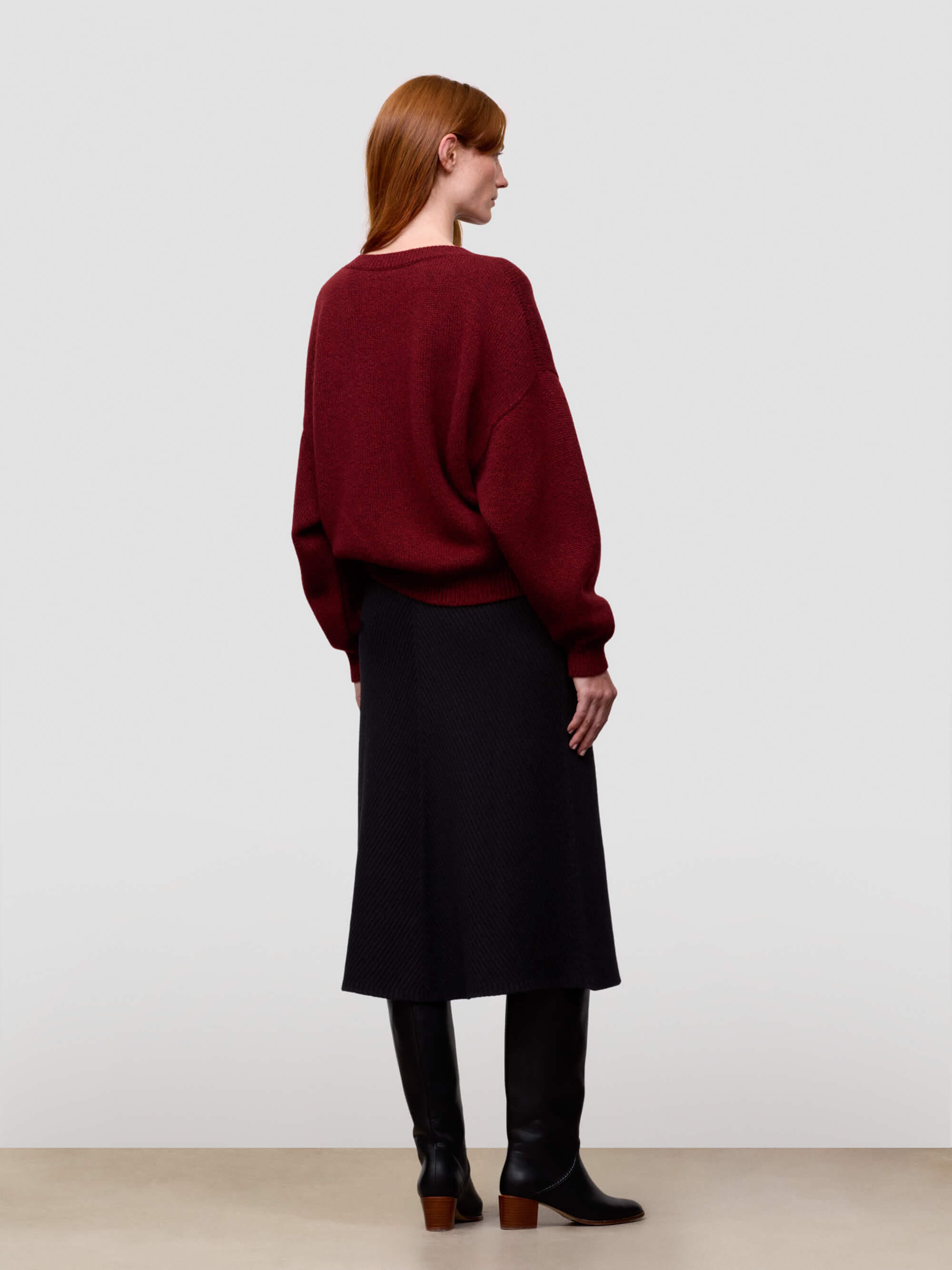 woman wearing a red chunky v-neck cashmere sweater and black cashmere skirt on a grey background