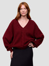 woman wearing a red chunky v-neck cashmere sweater and black cashmere skirt on a grey background